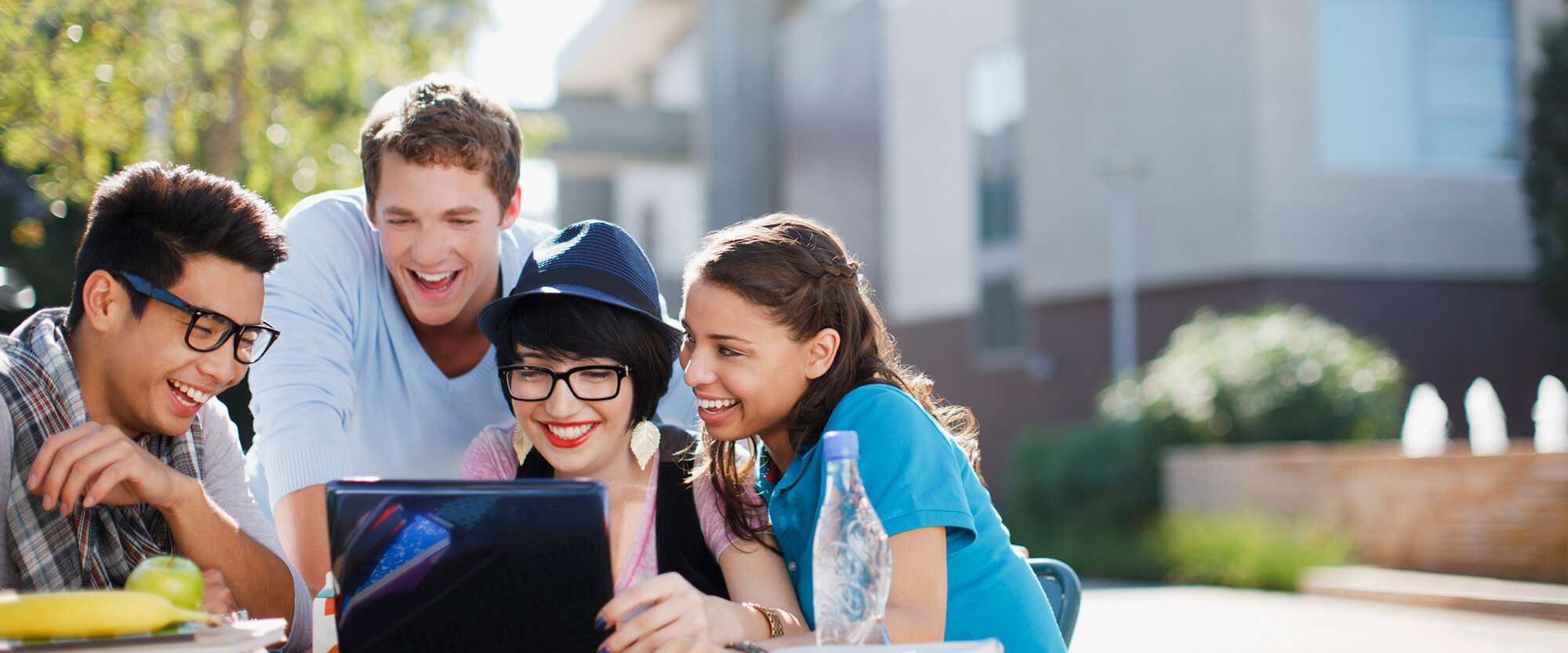 Students gathered around a laptop together, smiling.
