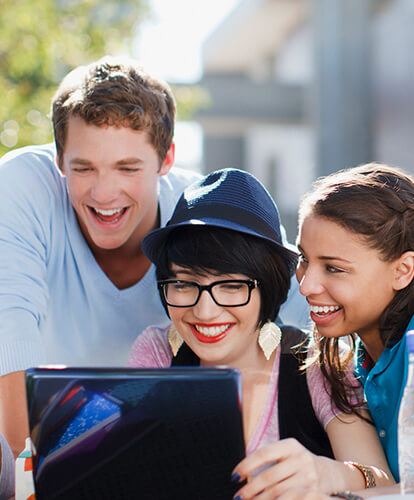 Smiling people gathered around a laptop.