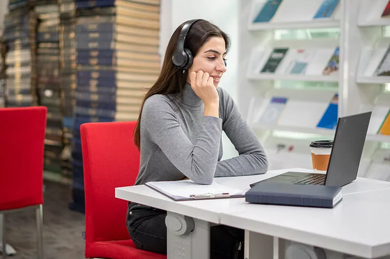 A student watches her laptop screen with headphones on.