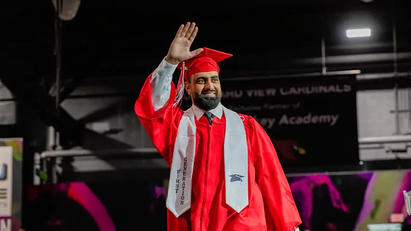 A first-generation student waves as he walks across the stage at Commencement.