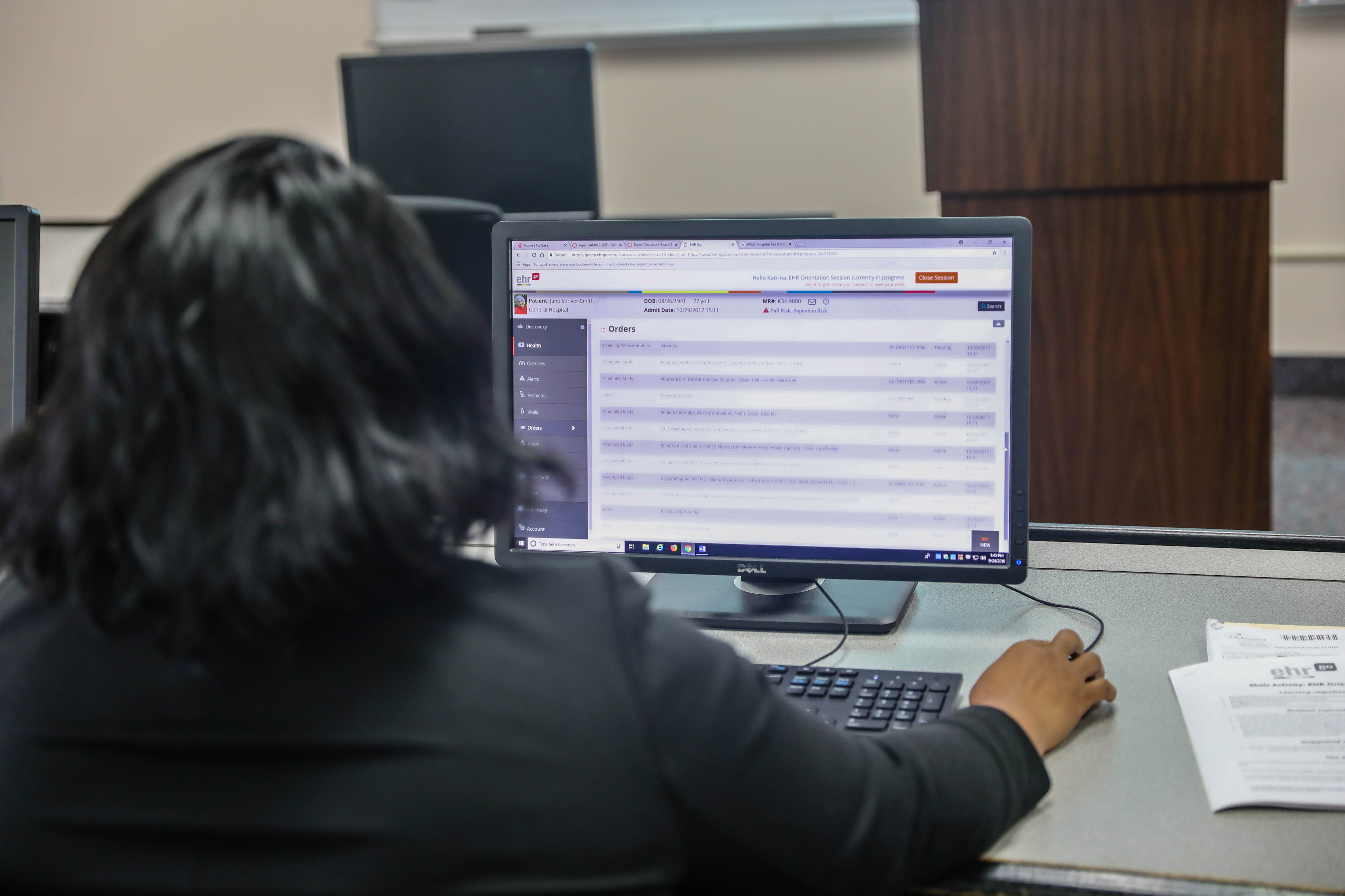 Baker College student facing a computer monitor that is displaying a medical record example.