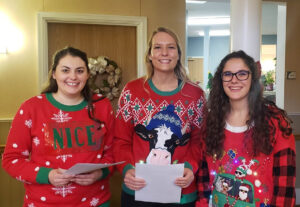 Three Baker College students wearing festive holiday sweaters