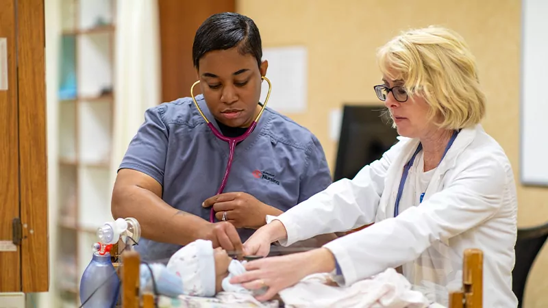 Nursing instructor and nursing student taking the pulse of a infant model.