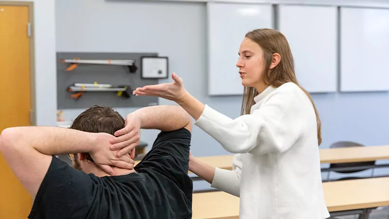 Female student leading a male student through a range-of-motion stretch.