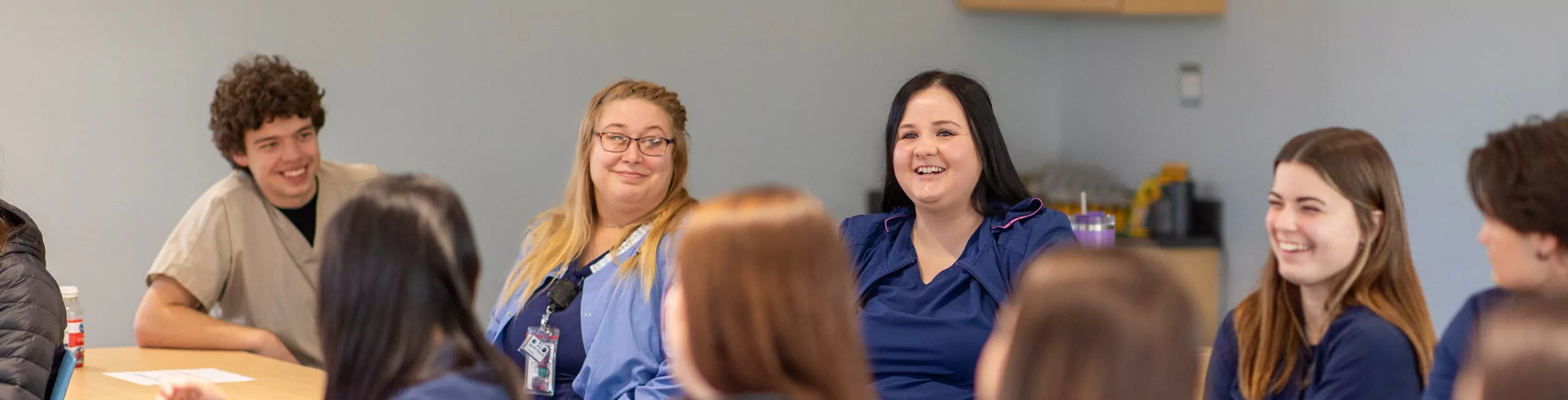 A group of students wearing scrubs listen during class.