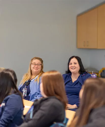 A group of students wearing scrubs listen during class.