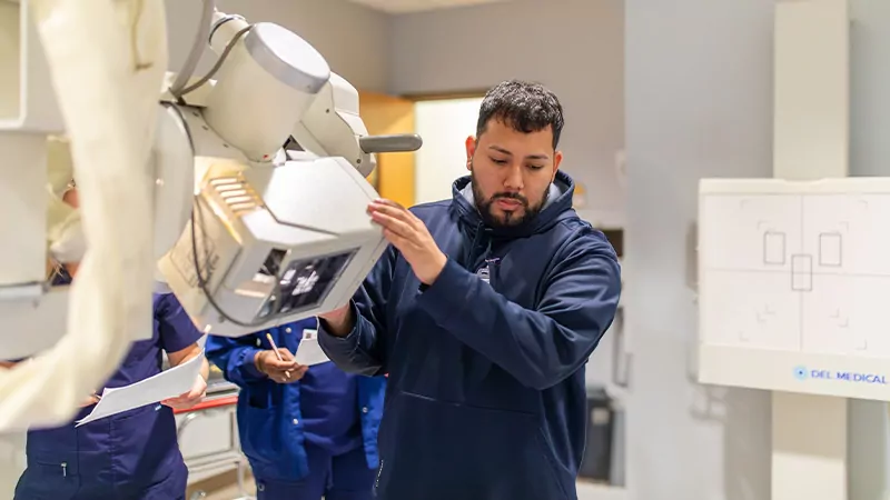 Male student utilizing digital radiography equipment in a campus lab.