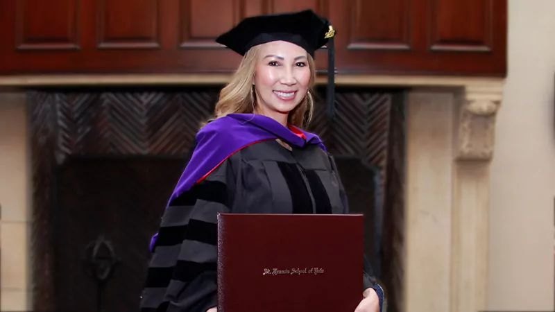 A law school graduate walks during Commencement as she smiles and holds a diploma case.