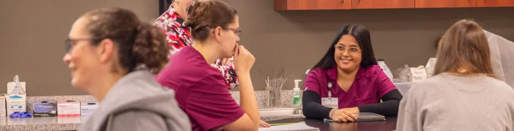 Happy Vet Tech students in scrubs chat in a lab class.