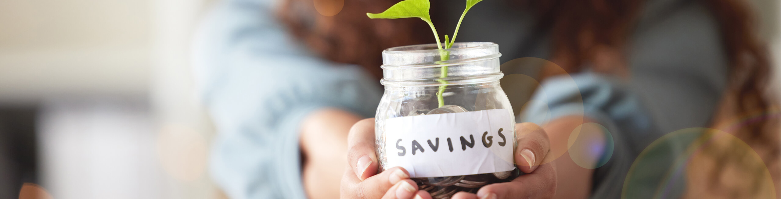 A woman holding a jar with a plant sprouting from it. The jar is labeled 'Savings'.