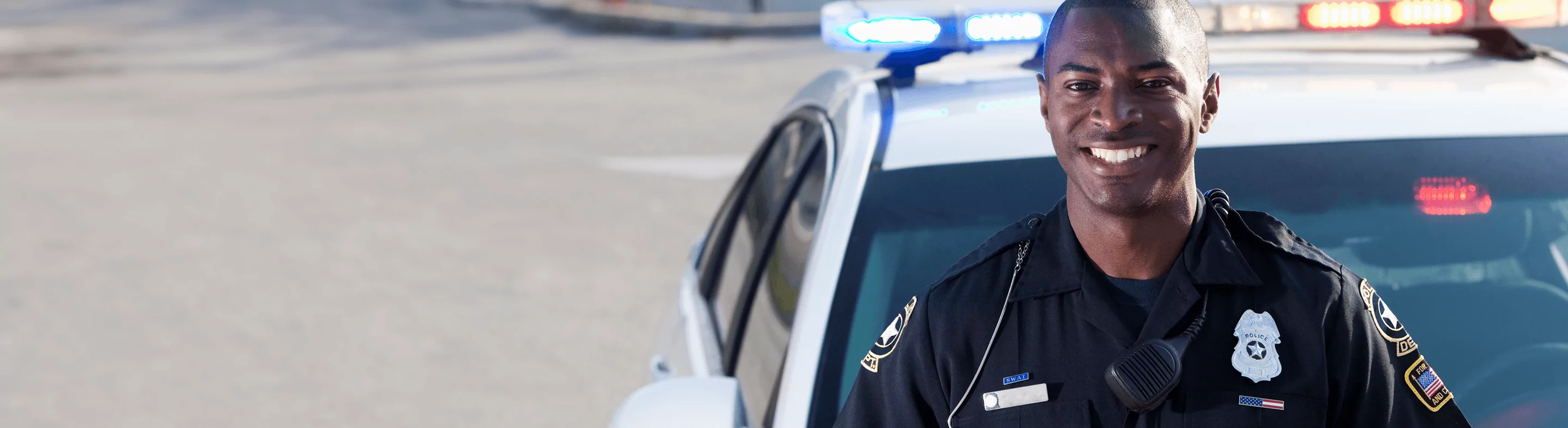 Friendly police officer smiles in front of police car