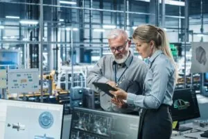Car Factory Office: Manager Talks with Senior Engineer, Use Tablet Computer to Design Production Conveyor for Advanced Power Engines.