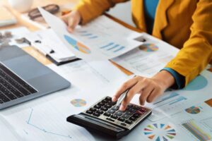 Woman accountant using calculator and computer holding a pen.