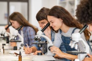 Group of college students performing experiment using microscope in science lab.