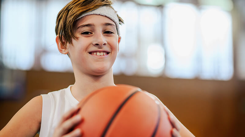 A child smiles while holding a basketball in both hands.