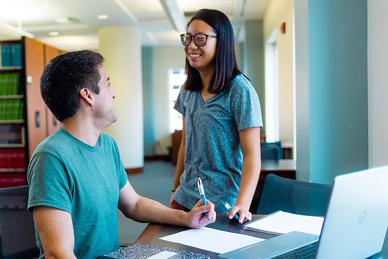 Two students talk as one takes notes.