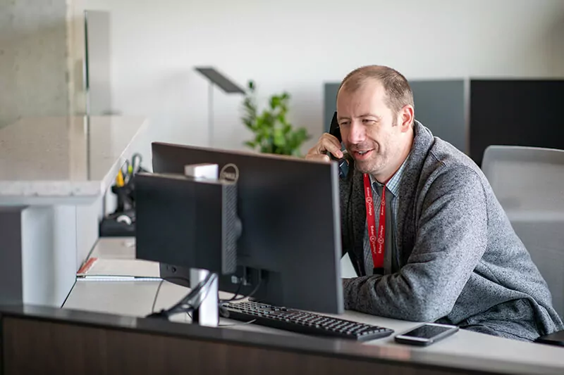 A man on the phone next to his computer.