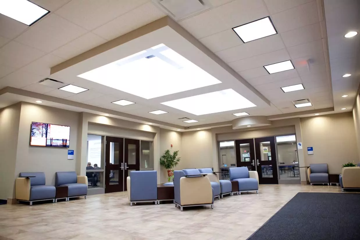 The lobby at the Baker College Cadillac campus, a well-lit room filled with comfy chairs with folding desk armrests. Around the edges of the room are doors to classrooms.