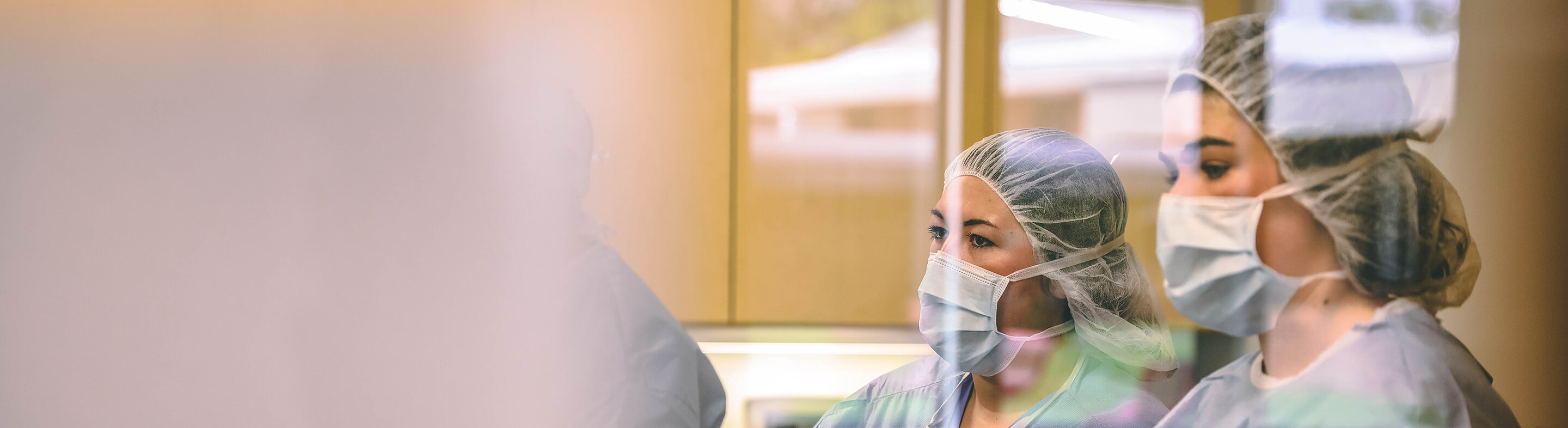 Two nursing students wearing scrubs watch during a lecture in a lab.