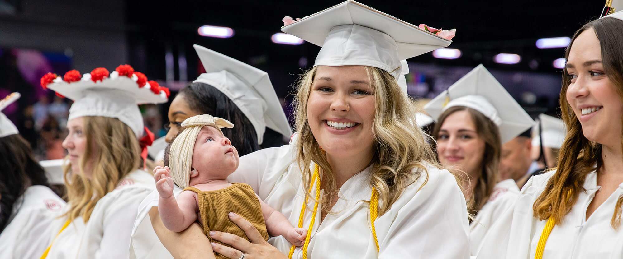 A graduate smiles as she holds her infant child during the ceremony.