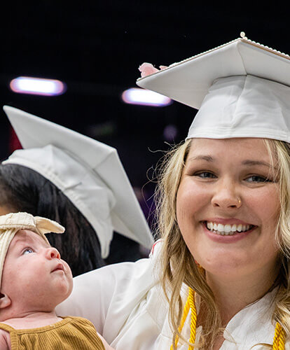 A graduate smiles as she holds her infant child during the ceremony.