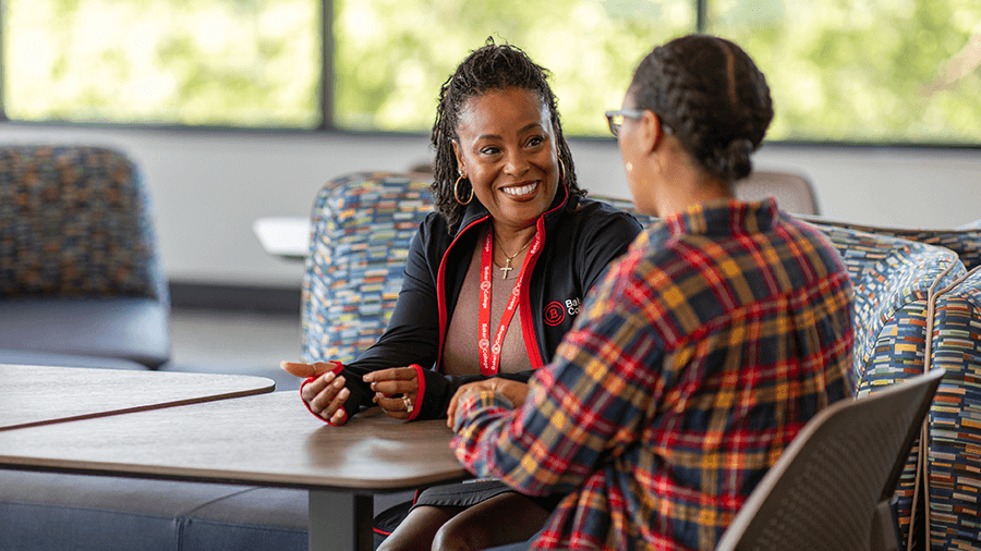 A counselor and a student talk at a table on campus.