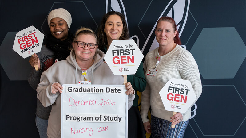 Four first-generation students gather in front of a Baker Bees backdrop.