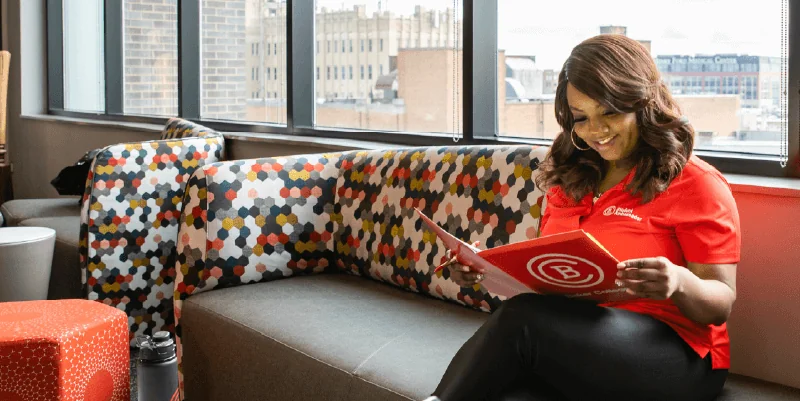 A woman in a red shirt holds a folder with the Baker College logo