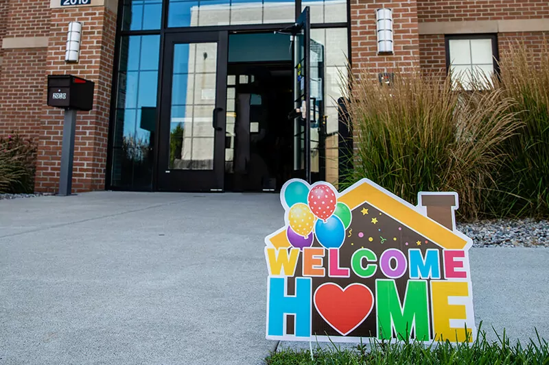 A "Welcome Home" sign with colorful balloons outside of a student housing building.