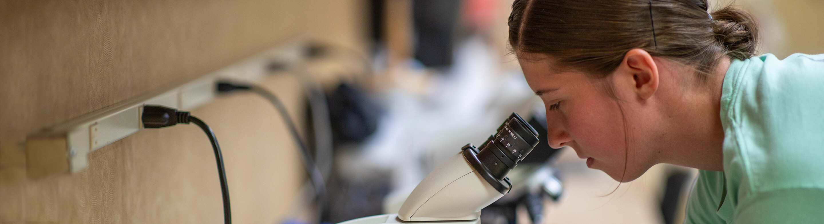 A student leans in to peer through a microscope in a lab.