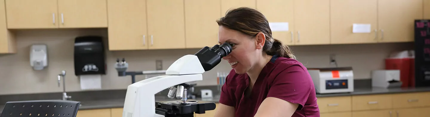 A student looks through a microscope in a classroom lab.