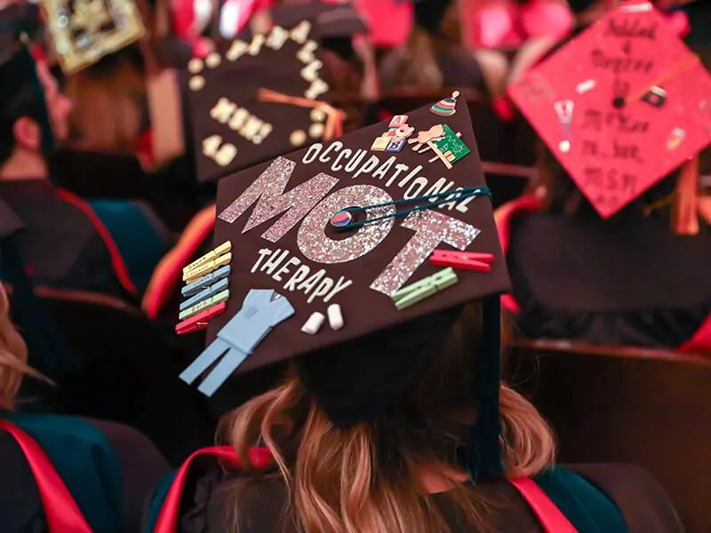 A graduation cap decorated with ribbons and clothespins and glittery text as seen from above