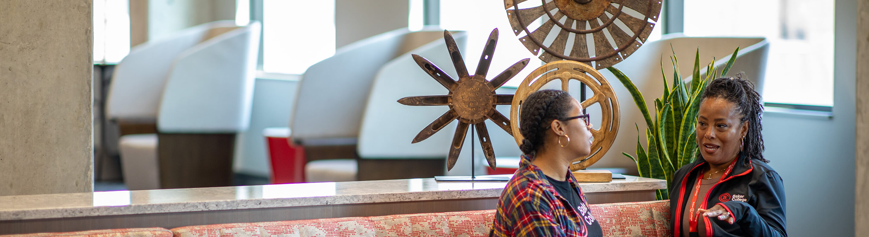 A staff member and a student converse on a couch on the Royal Oak campus.