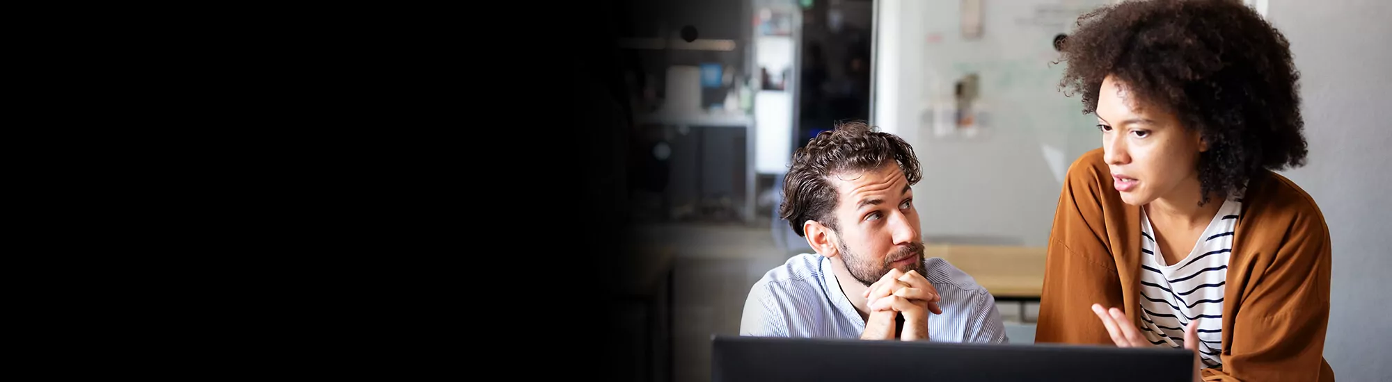 Two people discuss ideas near an open laptop screen.