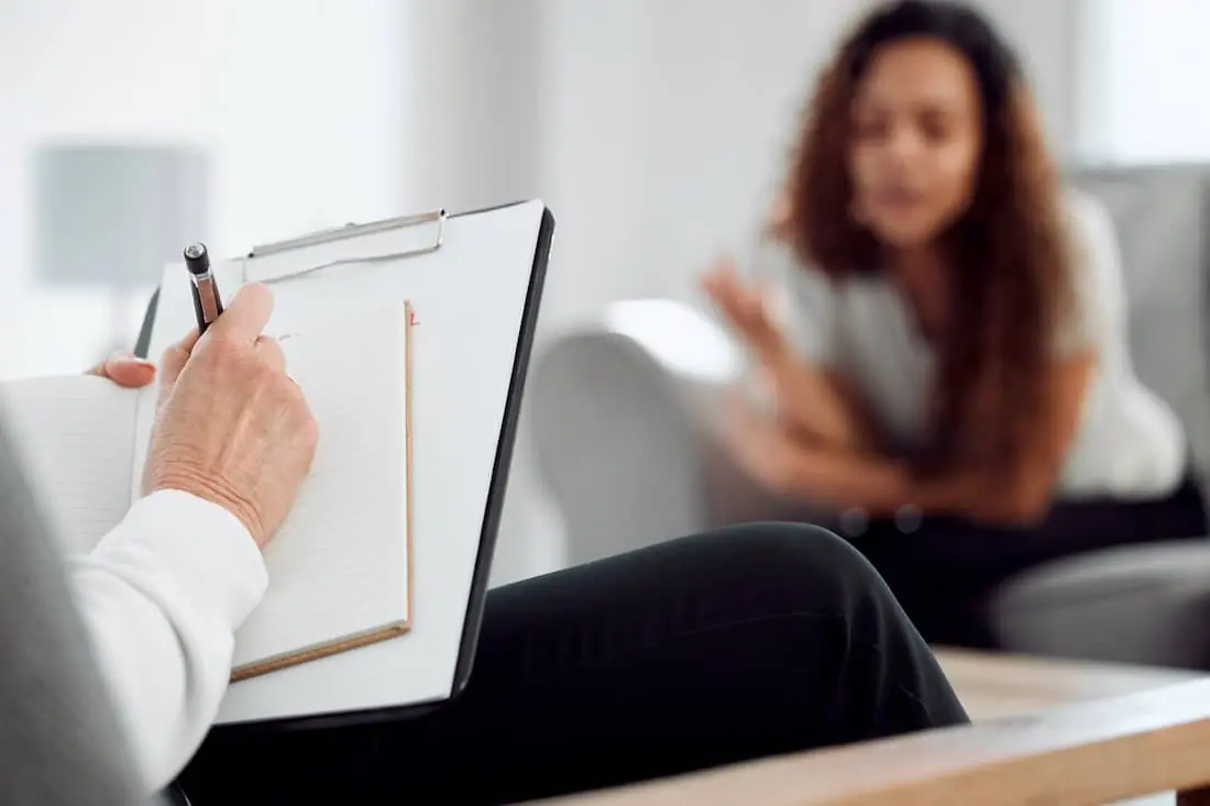 Psychologist writing in notebook with patient in consultation.