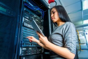 Young engineer businesswoman with tablet in network server room.