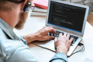 Over shoulder closeup view man IT programmer typing code develop program on screen web system app development concept.