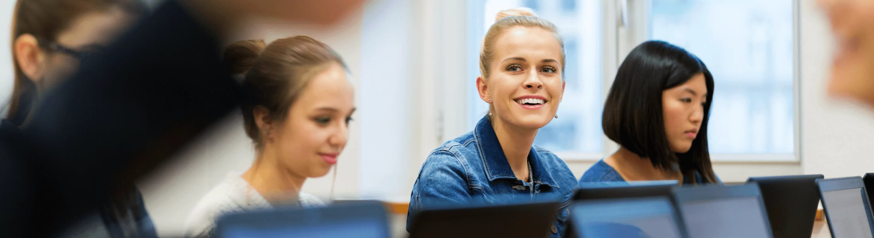 A woman smiles while looking up from her computer in class.