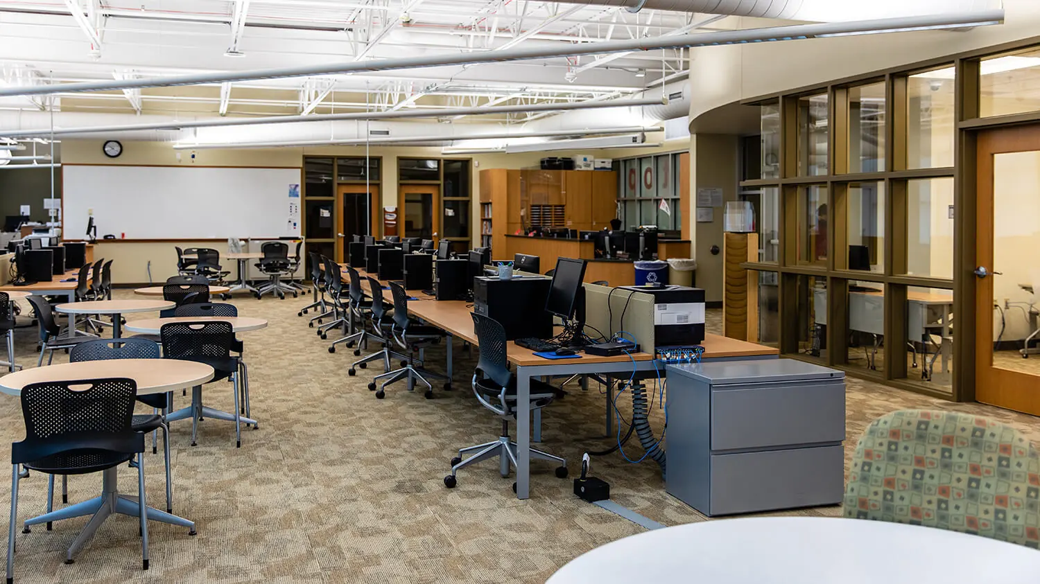 An interior photo of the Jackson campus featuring several circular tables with chairs and a row of computer workstations.