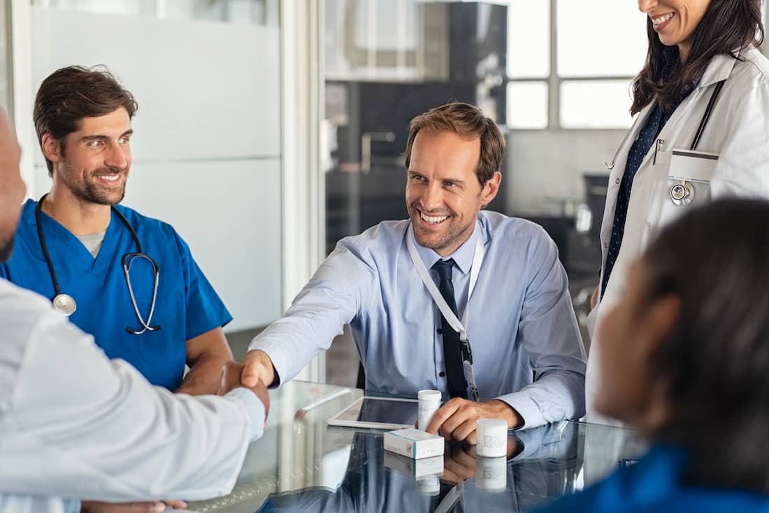 Healthcare manager shaking hands with doctor in meeting room.