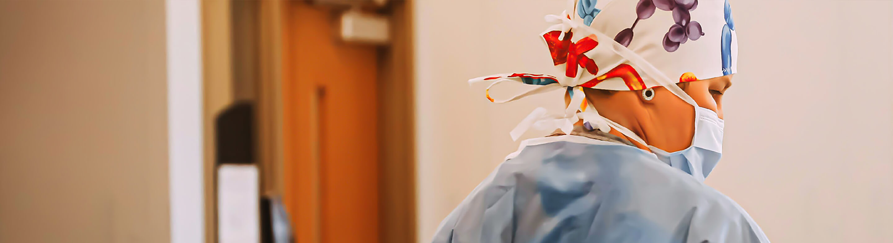 A nurse wearing scrubs and a respiratory mask works at a desk in a healthcare facility.