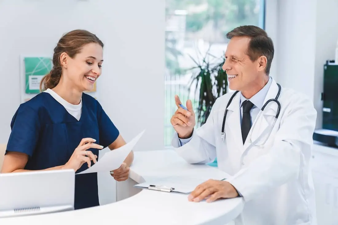 Senior doctor talking with nurse administrator at hospital reception.