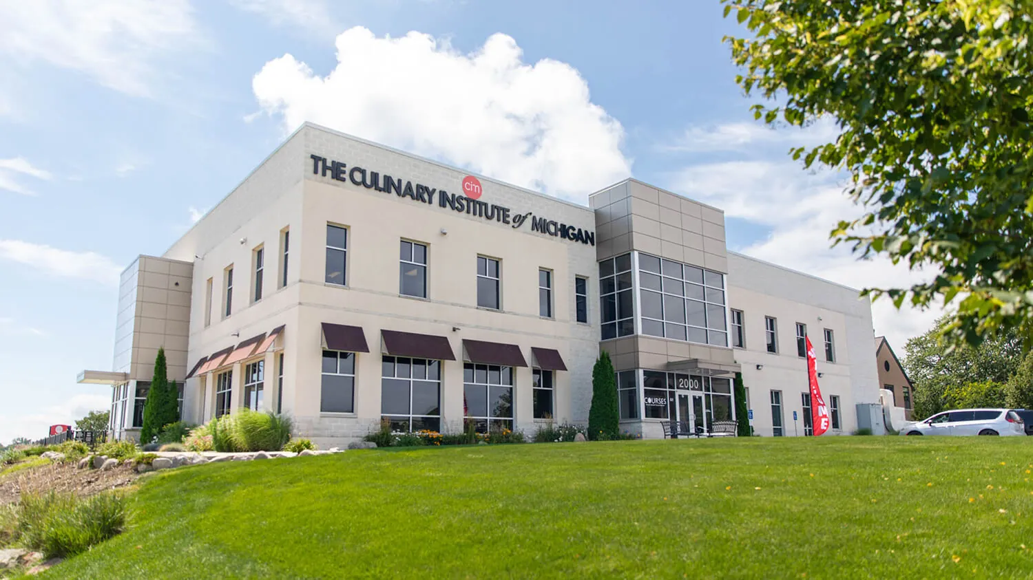 An exterior photo of the Culinary Institute of Michigan building, in the sun on a grassy hill against a blue sky
