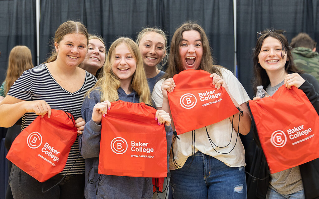 Students smile at the camera while holding Baker bags