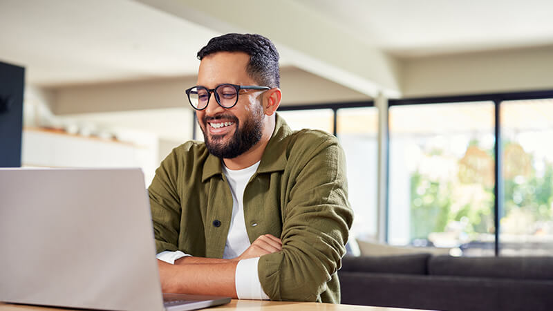 A man smiles as he watches an online course on his laptop.