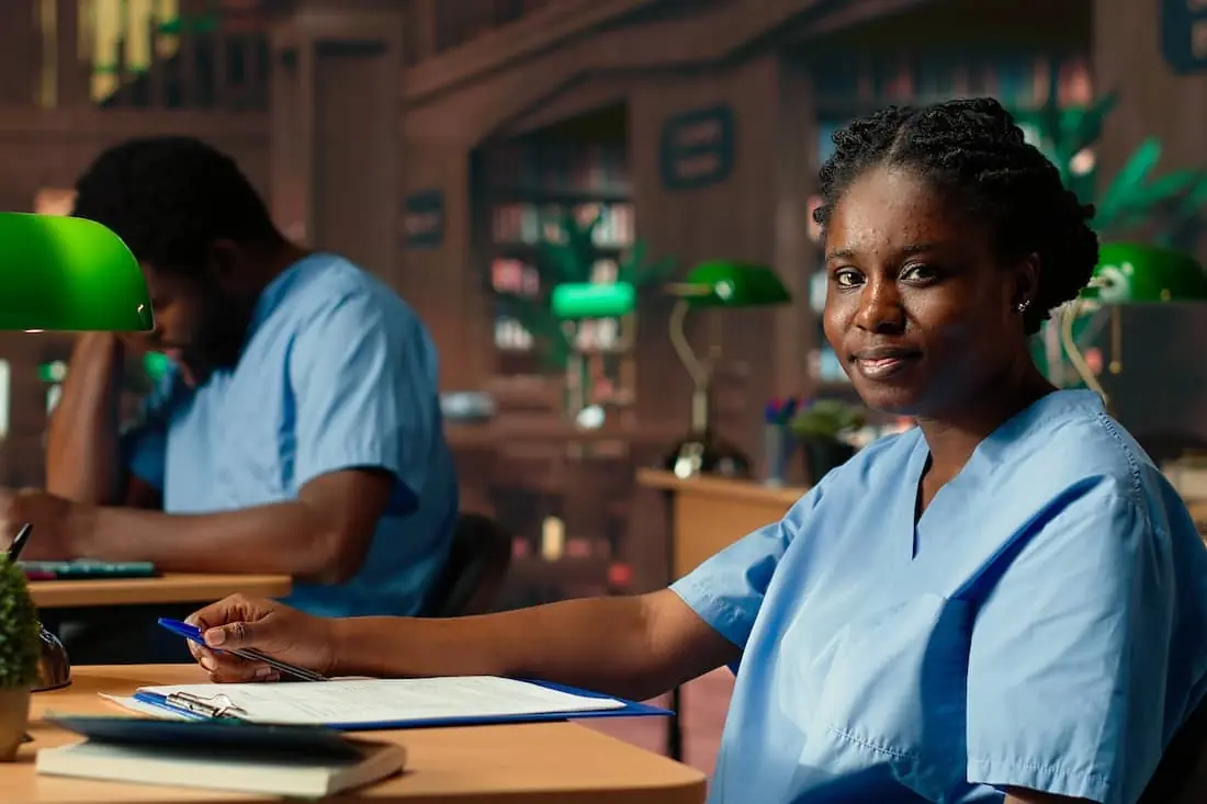 Girl in scrubs works hard on nursing school success in library.