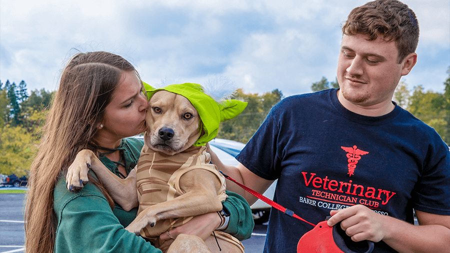 Two students hold a puppy. The student on the right wears a Veterinary Technician Club shirt.