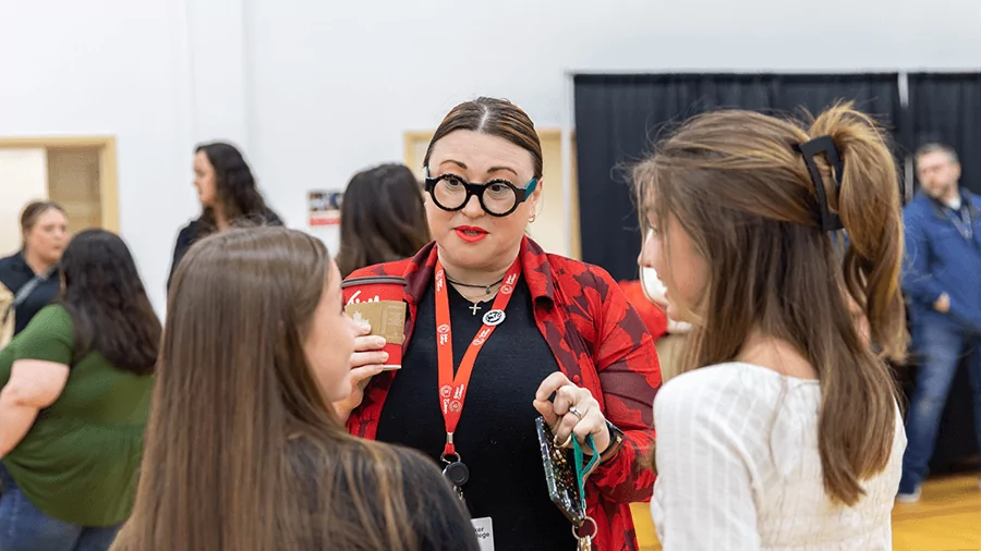 The Dean of Students, a woman wearing a red Baker lanyard, speaks with a group of students at an event.