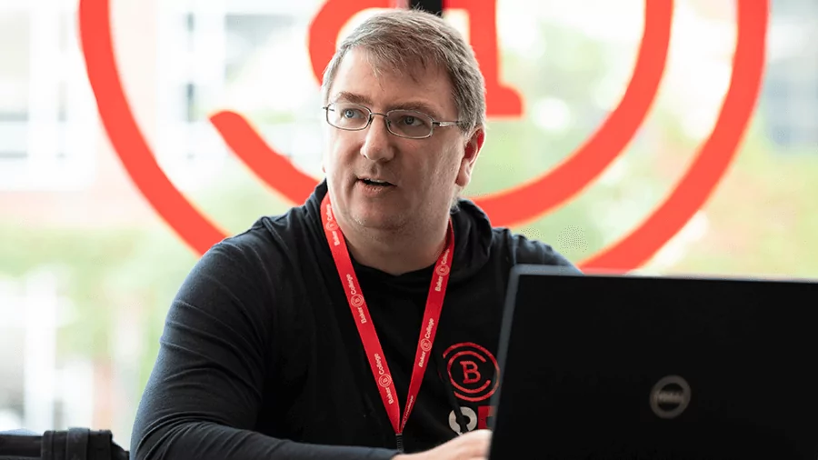 An IT staff member works on a laptop while sitting in front of the Baker logo.