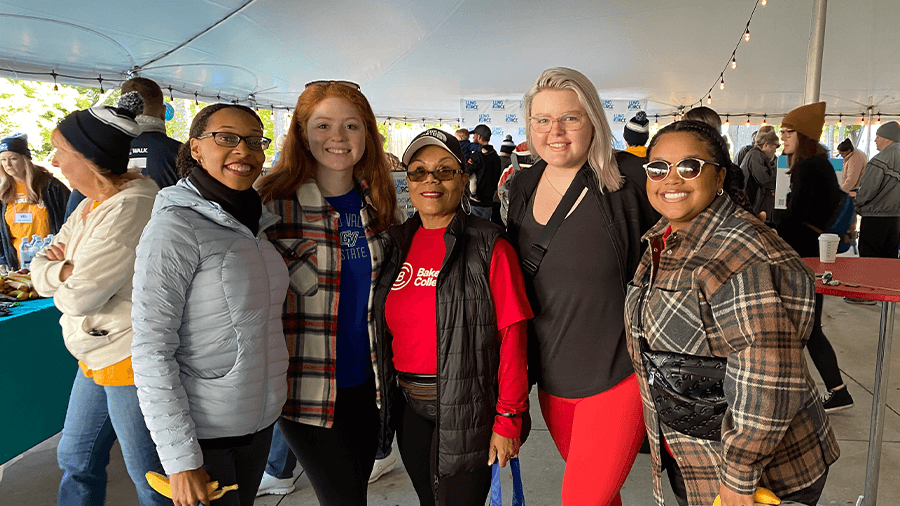 A diverse group of students standing in a tent during an event and smiling.